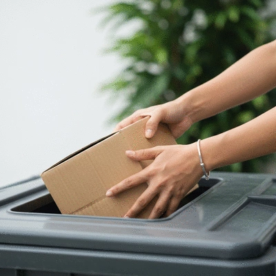 Hands placing cardboard into a recycling bin with a green background